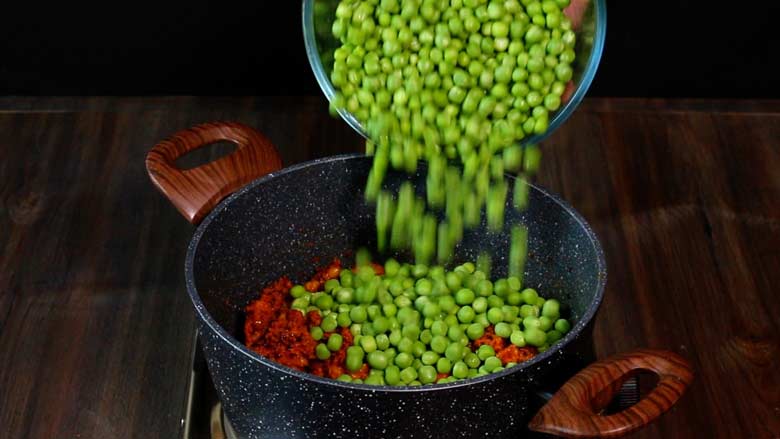 Freshly shelled green peas are being tipped into a non stick pan with the walnut masala to make Malvani Green Peas Curry - Malvani Green Peas and Walnut Curry Recipe